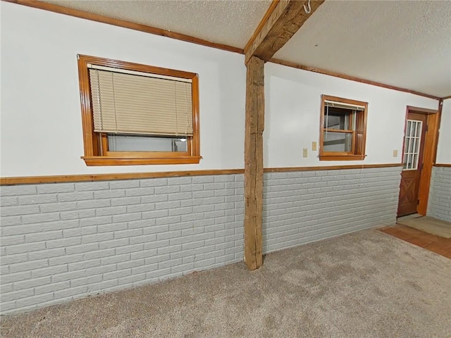 carpeted spare room with beamed ceiling, brick wall, a textured ceiling, and ornamental molding