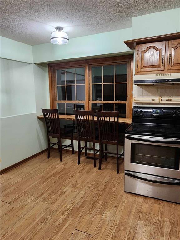 kitchen with a textured ceiling, under cabinet range hood, electric range, baseboards, and light wood-type flooring