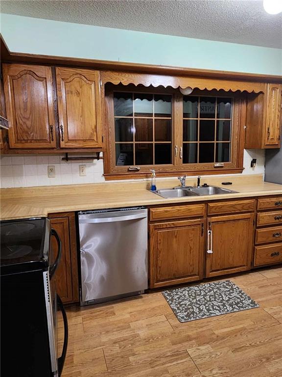kitchen featuring a textured ceiling, a sink, light wood-type flooring, light countertops, and appliances with stainless steel finishes