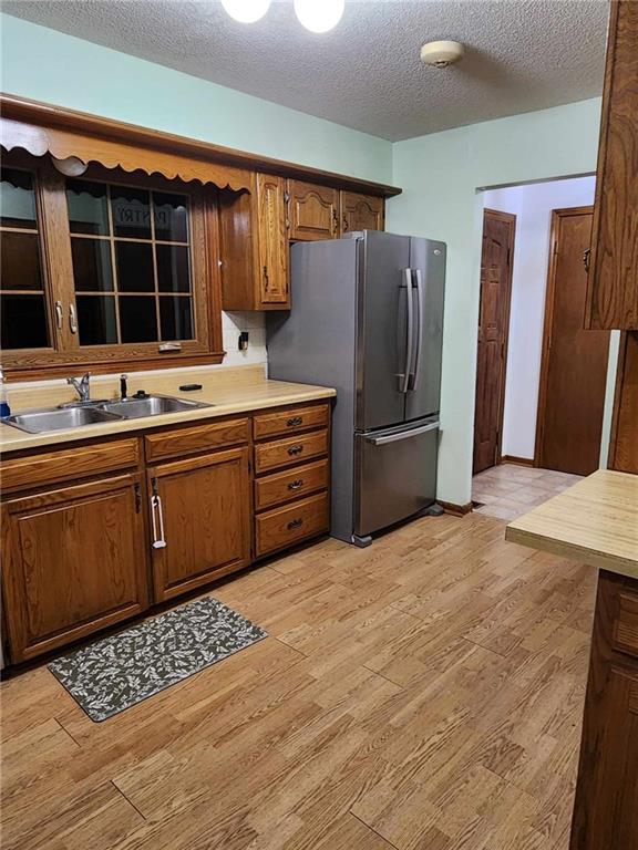 kitchen with a textured ceiling, a sink, light wood finished floors, light countertops, and freestanding refrigerator