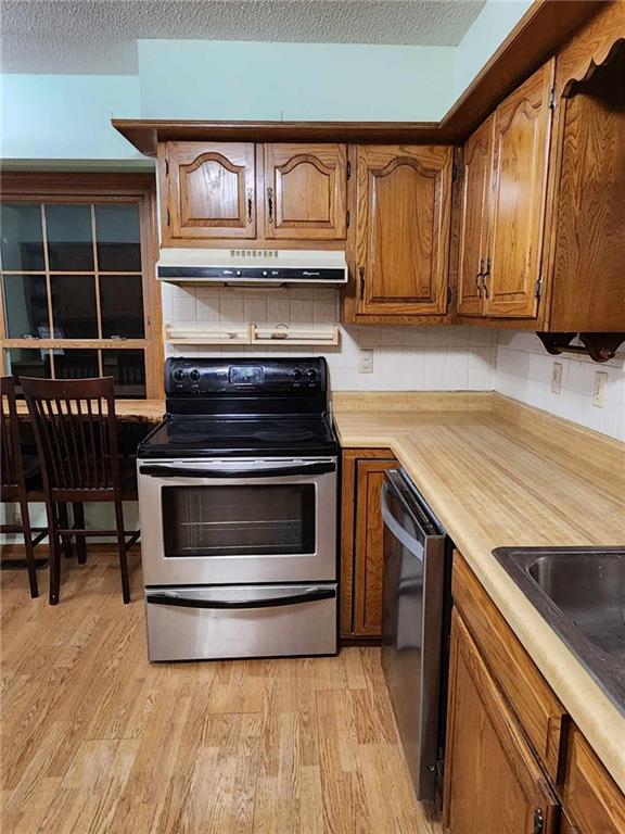 kitchen featuring a textured ceiling, light countertops, appliances with stainless steel finishes, light wood finished floors, and under cabinet range hood