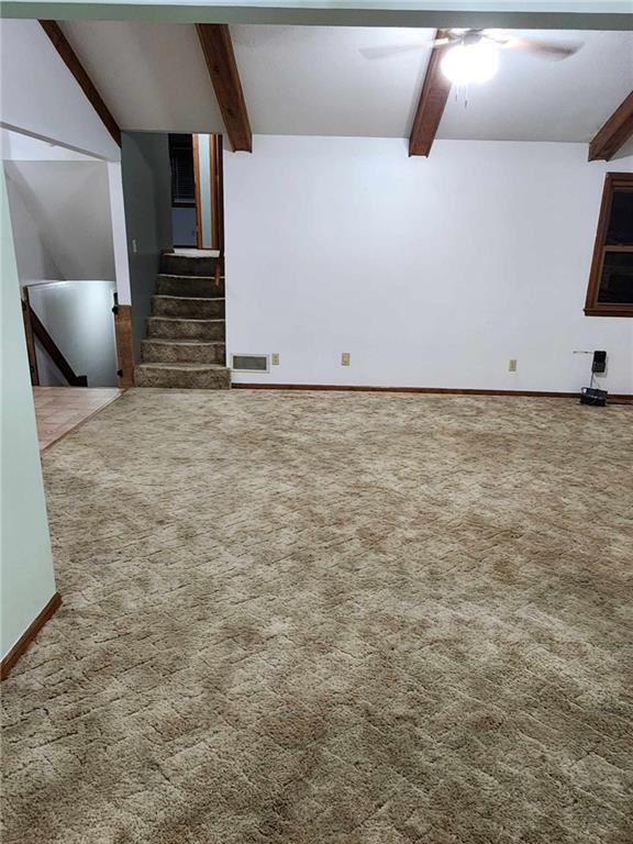 unfurnished living room with carpet floors, beam ceiling, and a ceiling fan