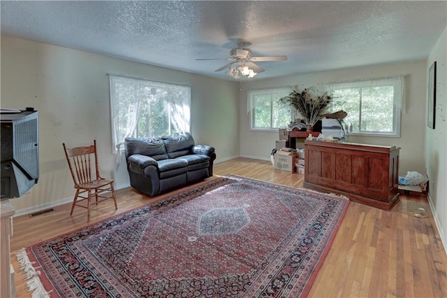 living room with a textured ceiling, light wood-type flooring, and ceiling fan