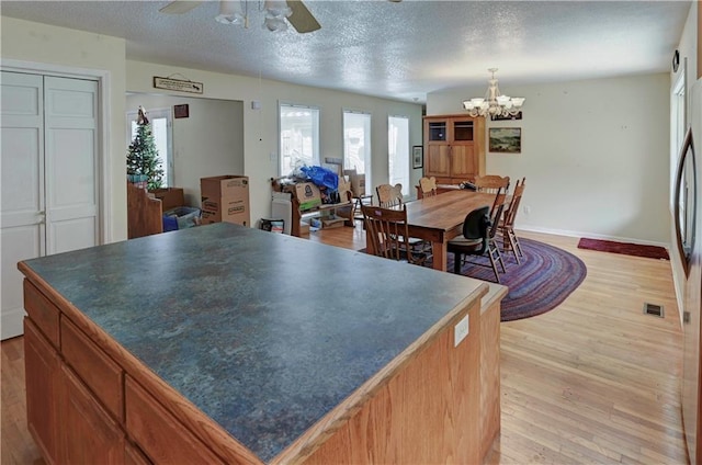 kitchen with hanging light fixtures, a kitchen island, a textured ceiling, light wood-type flooring, and ceiling fan with notable chandelier