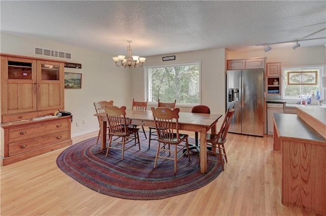 dining space with a textured ceiling, light hardwood / wood-style flooring, a chandelier, and track lighting