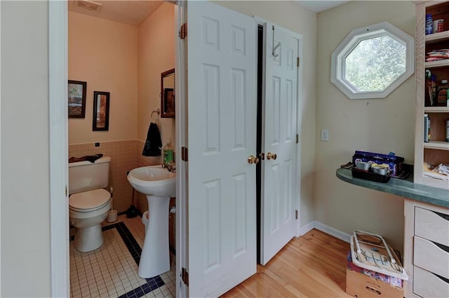 bathroom with toilet, hardwood / wood-style flooring, tile walls, and sink