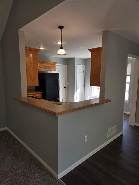 kitchen with pendant lighting, black fridge, sink, dark hardwood / wood-style flooring, and kitchen peninsula