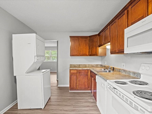 kitchen with white appliances, stacked washer / drying machine, sink, and light hardwood / wood-style floors