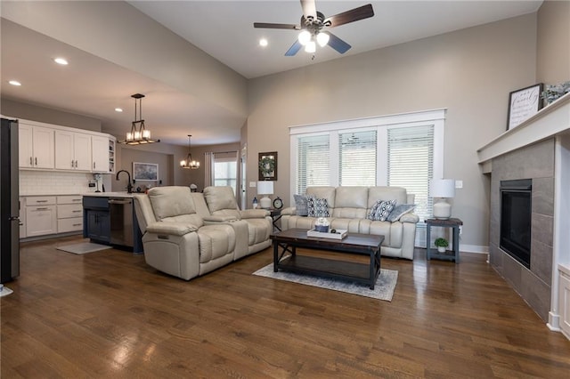 living room featuring sink, a tiled fireplace, dark hardwood / wood-style flooring, and ceiling fan with notable chandelier