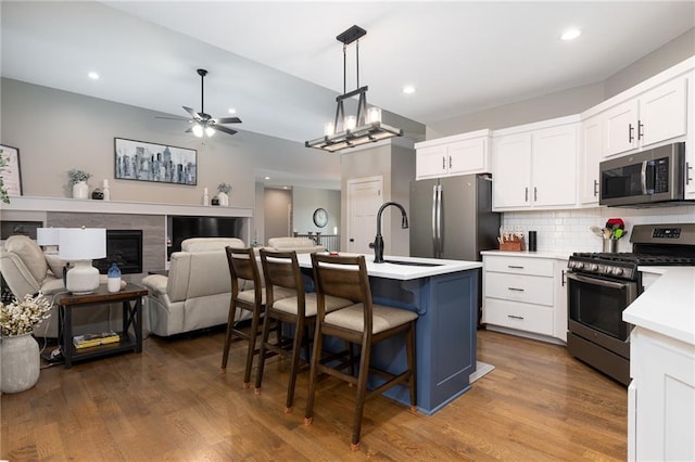 kitchen featuring dark hardwood / wood-style floors, an island with sink, white cabinets, a kitchen bar, and appliances with stainless steel finishes