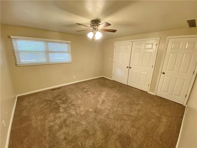 unfurnished bedroom with dark carpet, two closets, and ceiling fan