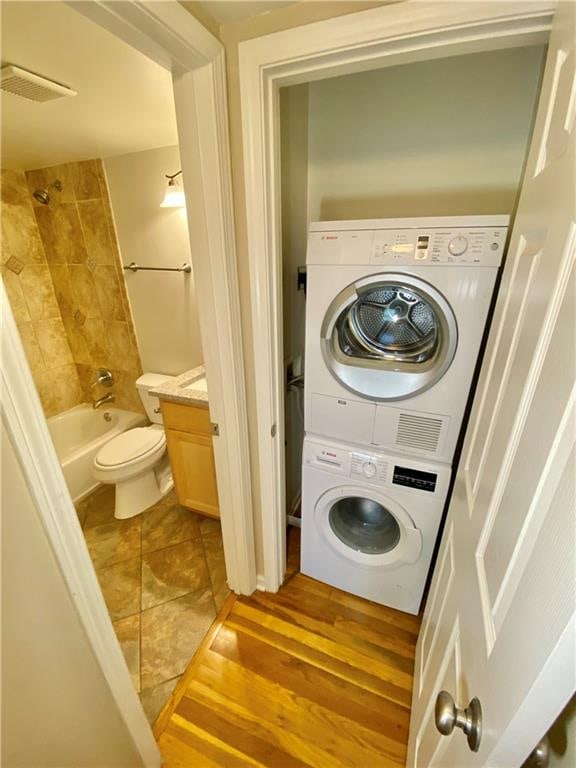 laundry room featuring stacked washer / drying machine and light wood-type flooring