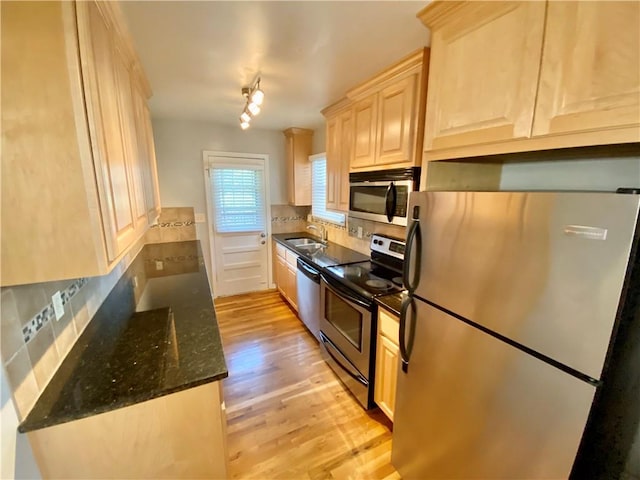 kitchen with dark stone countertops, sink, light wood-type flooring, light brown cabinetry, and appliances with stainless steel finishes