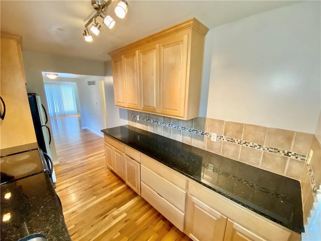 kitchen with tasteful backsplash, light brown cabinetry, light hardwood / wood-style floors, dark stone counters, and track lighting