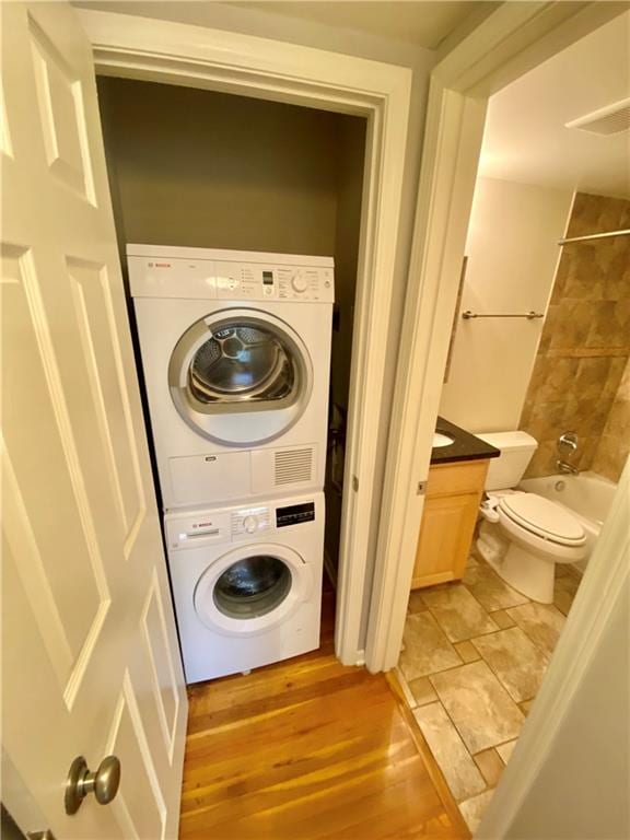 clothes washing area with hardwood / wood-style floors and stacked washer / dryer