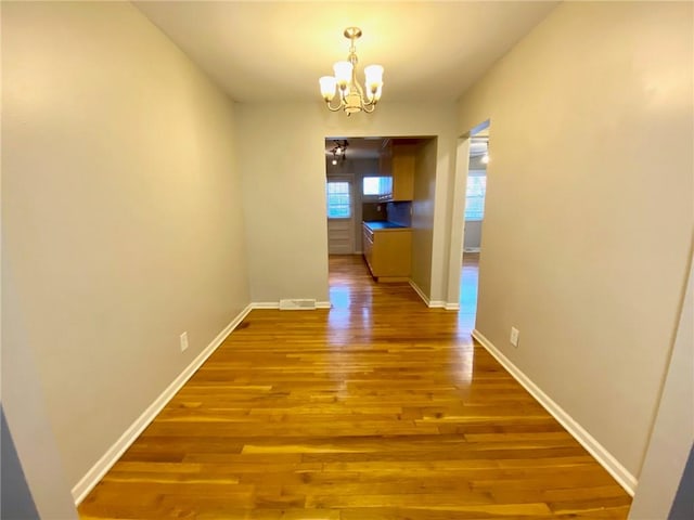 hallway featuring wood-type flooring and an inviting chandelier