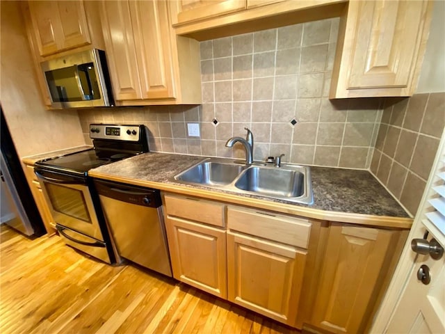 kitchen with sink, stainless steel appliances, light wood-type flooring, and tasteful backsplash