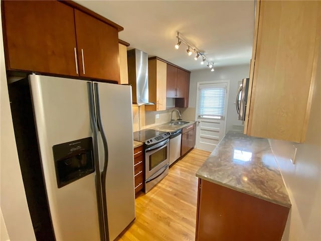 kitchen featuring light stone countertops, light wood-type flooring, sink, wall chimney exhaust hood, and stainless steel appliances