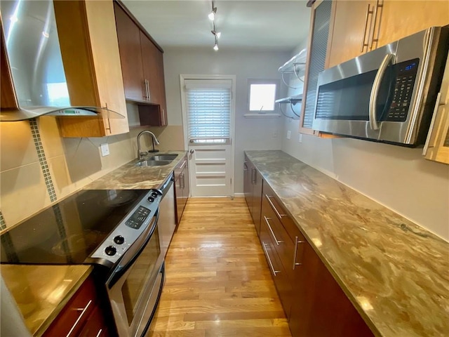 kitchen featuring sink, light wood-type flooring, stainless steel appliances, range hood, and light stone counters