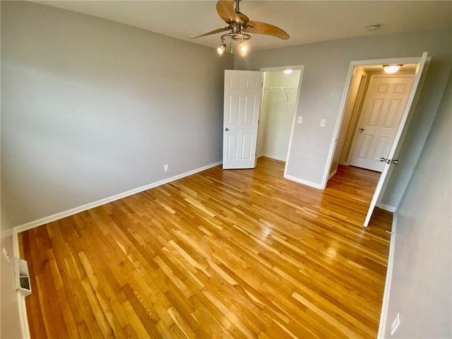 unfurnished bedroom featuring a closet, ceiling fan, light wood-type flooring, and a walk in closet