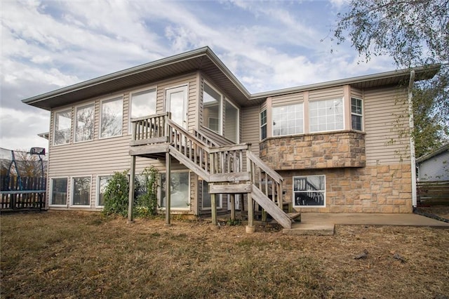 403 S Jackson St, Archie, MO 64725 - rear view of house featuring stone siding, stairs, and a trampoline