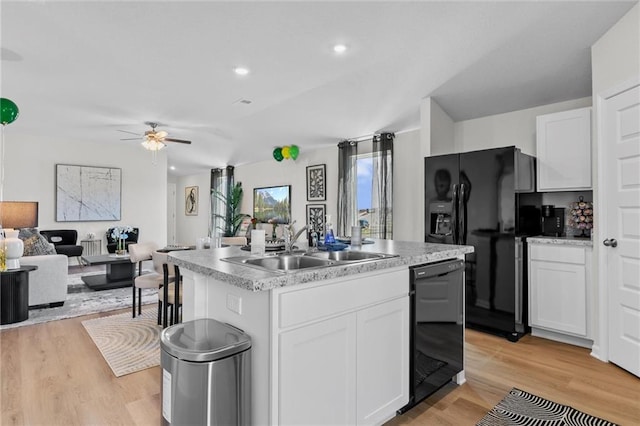 kitchen with white cabinets, black appliances, a kitchen island with sink, and light hardwood / wood-style flooring