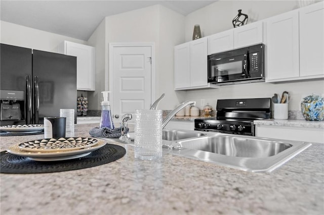 kitchen with black appliances, white cabinetry, and vaulted ceiling