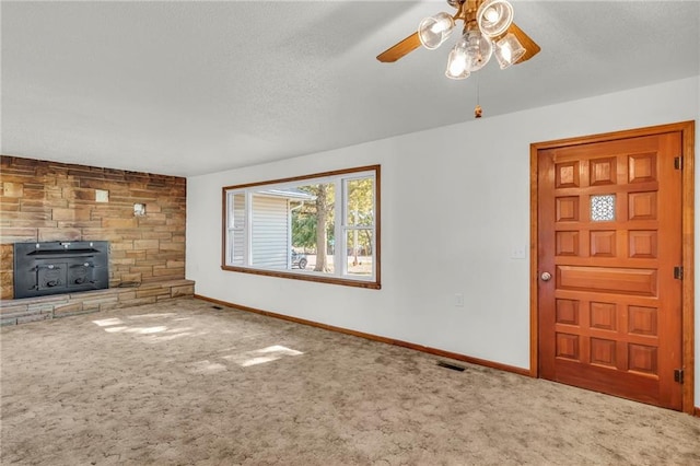 unfurnished living room featuring carpet flooring, a wood stove, a textured ceiling, and ceiling fan