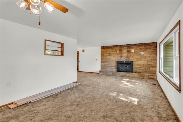 unfurnished living room with carpet, a wood stove, and ceiling fan