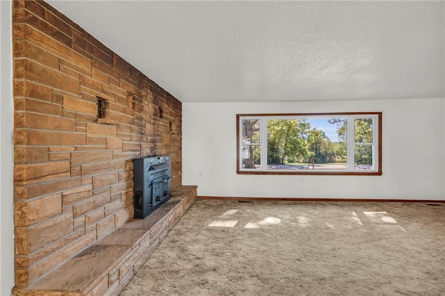 unfurnished living room with carpet flooring, a wood stove, and a textured ceiling