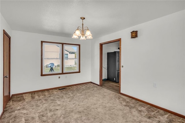 carpeted spare room featuring a notable chandelier and a textured ceiling