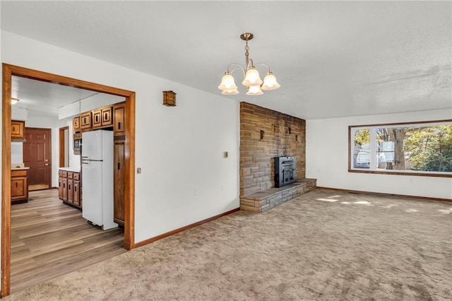 unfurnished living room with an inviting chandelier, a wood stove, and wood-type flooring