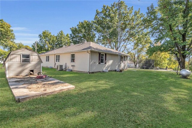 rear view of property featuring central air condition unit, a lawn, and a trampoline