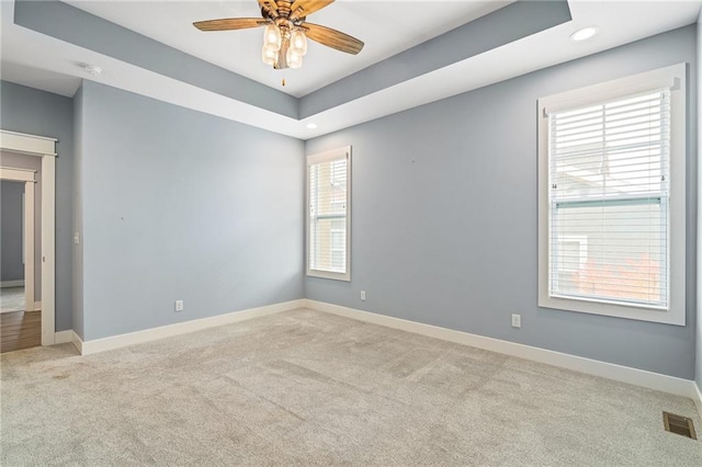 spare room with ceiling fan, light colored carpet, and a raised ceiling