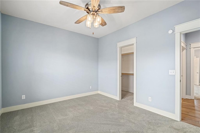 unfurnished bedroom with ceiling fan, a walk in closet, a closet, and light colored carpet