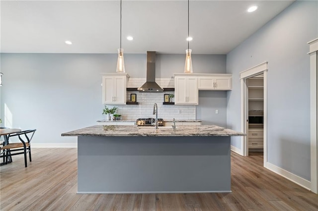 kitchen featuring decorative light fixtures, white cabinets, ventilation hood, and a center island with sink