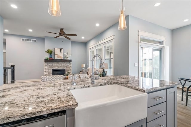 kitchen with decorative light fixtures, sink, dishwasher, and a stone fireplace