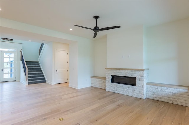 2852 W 133rd Ter, Leawood, KS 66209 - unfurnished living room with stairway, light wood-style flooring, a stone fireplace, a ceiling fan, and recessed lighting