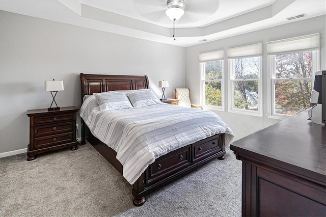 bedroom featuring a tray ceiling, light carpet, and ceiling fan