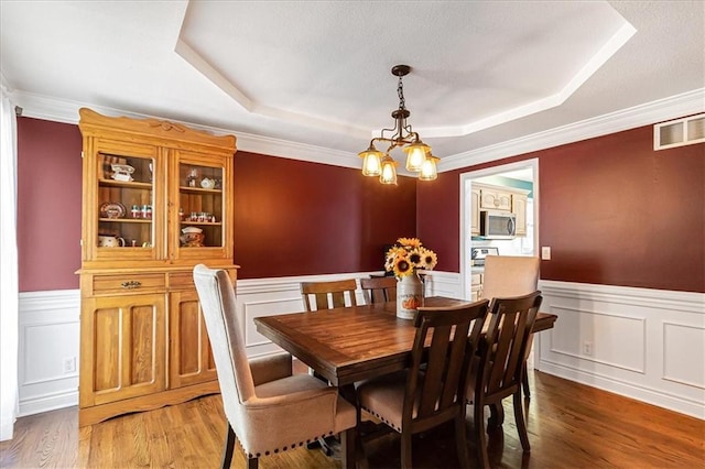 dining room featuring a chandelier, hardwood / wood-style floors, a raised ceiling, and crown molding