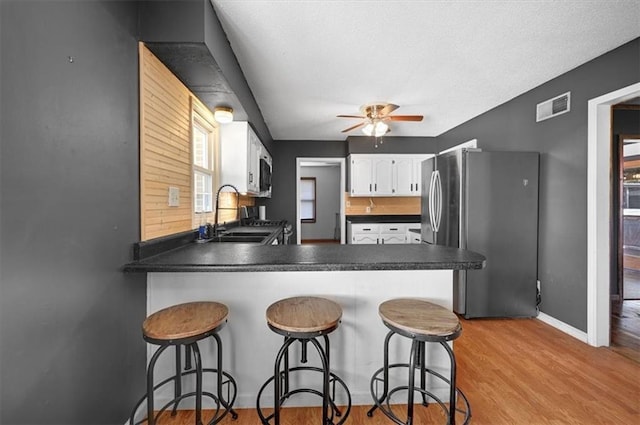 kitchen with a kitchen breakfast bar, kitchen peninsula, white cabinets, appliances with stainless steel finishes, and ceiling fan