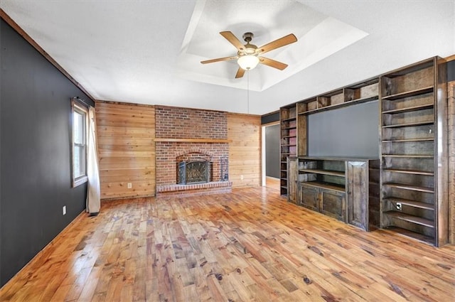 unfurnished living room featuring wooden walls, a fireplace, light hardwood / wood-style floors, and ceiling fan