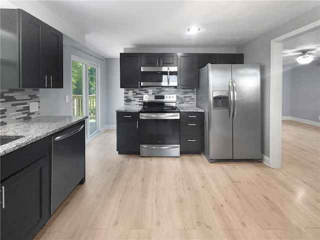 kitchen featuring backsplash, appliances with stainless steel finishes, light stone counters, and light wood-type flooring