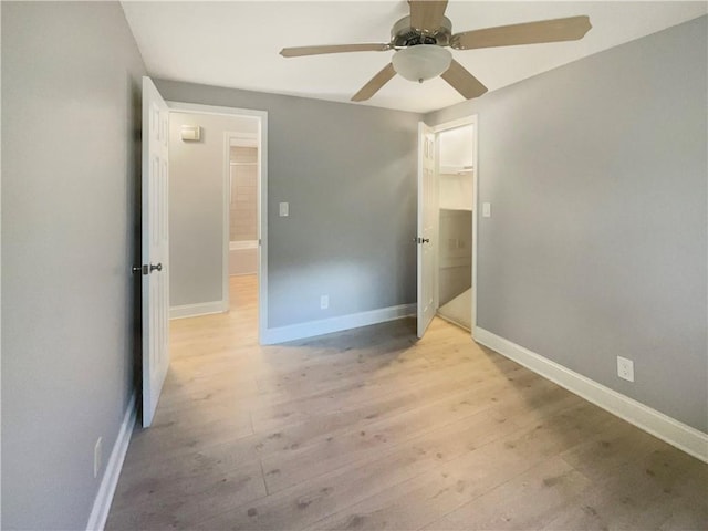 unfurnished bedroom featuring a closet, a walk in closet, light hardwood / wood-style floors, and ceiling fan