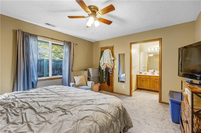 bedroom with light carpet, a textured ceiling, connected bathroom, and ceiling fan