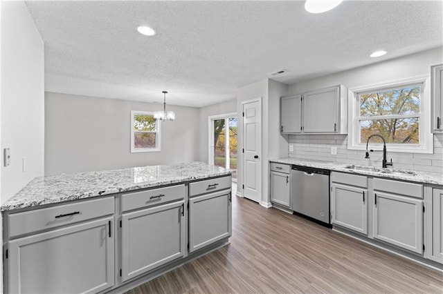 kitchen featuring sink, stainless steel dishwasher, dark wood-type flooring, decorative backsplash, and an inviting chandelier