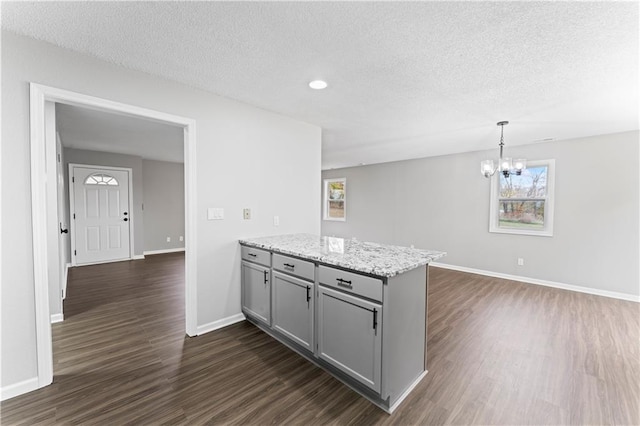 kitchen with dark wood-type flooring, gray cabinetry, light stone countertops, decorative light fixtures, and an inviting chandelier