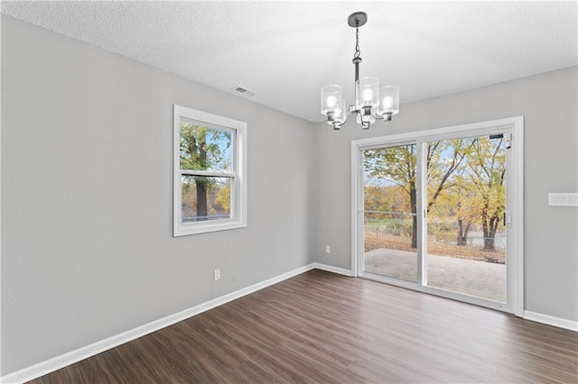 unfurnished room with a notable chandelier, a textured ceiling, dark hardwood / wood-style flooring, and plenty of natural light