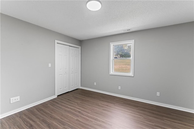 unfurnished bedroom featuring a closet, a textured ceiling, and dark hardwood / wood-style flooring