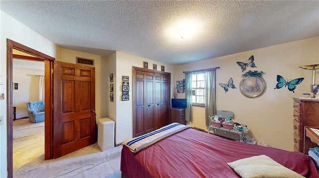 bedroom with a textured ceiling, light colored carpet, and a closet